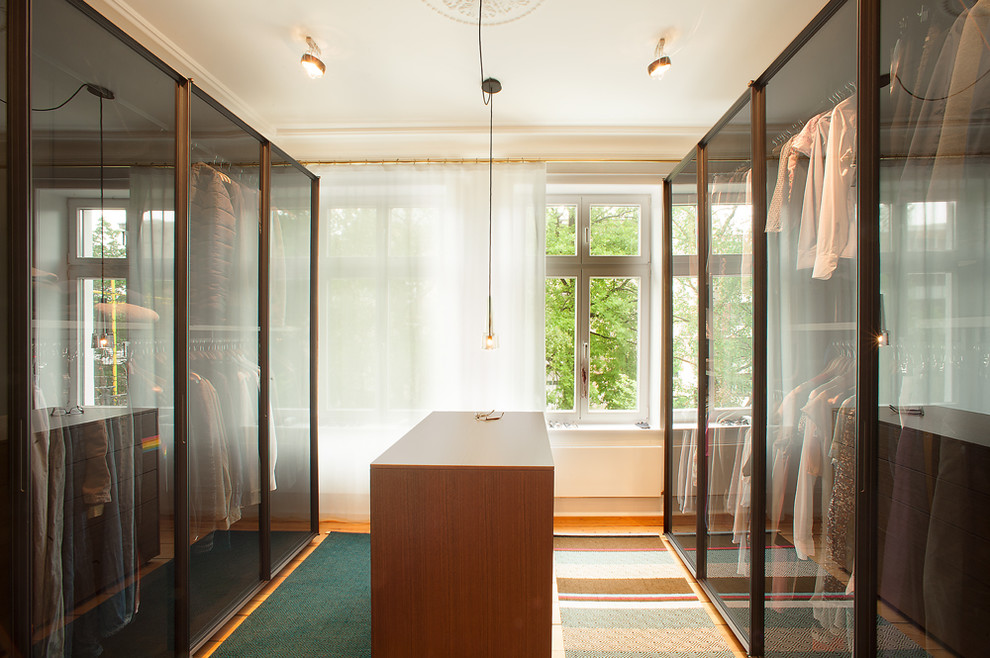 На фото: большая гардеробная комната унисекс в современном стиле с стеклянными фасадами и паркетным полом среднего тона с