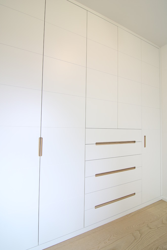 Foto di un armadio o armadio a muro unisex contemporaneo di medie dimensioni con ante lisce, ante bianche e parquet chiaro