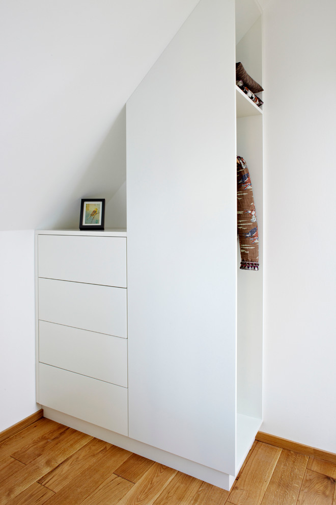 Modelo de armario unisex minimalista pequeño con armarios con paneles lisos, puertas de armario blancas y suelo de madera en tonos medios