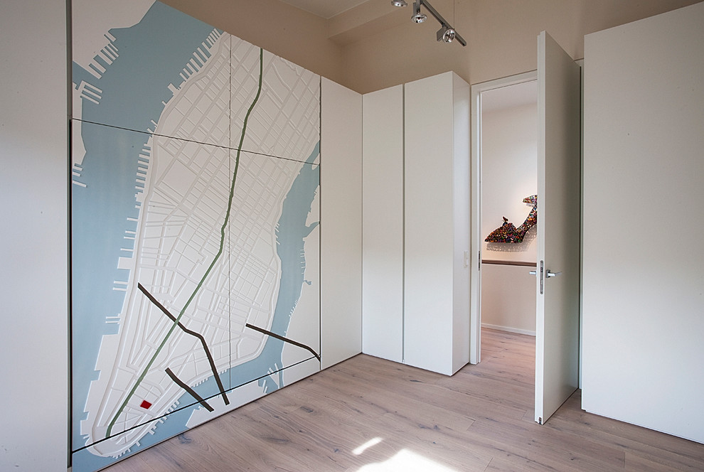 This is an example of a medium sized contemporary gender neutral dressing room in Munich with medium hardwood flooring, raised-panel cabinets and white cabinets.