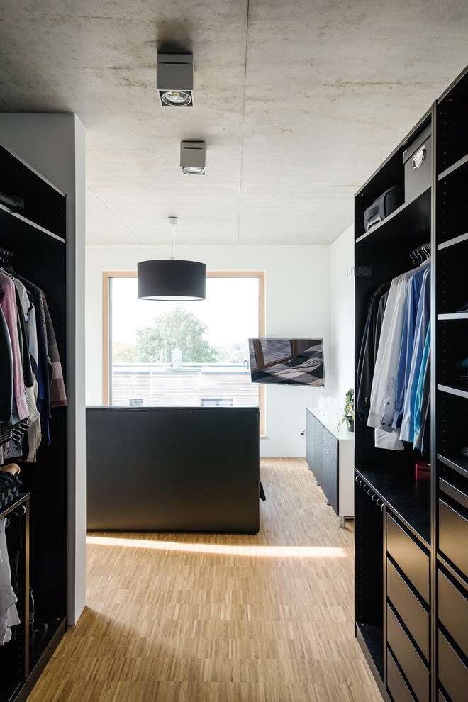 Foto de vestidor unisex moderno de tamaño medio con armarios abiertos, puertas de armario negras y suelo de madera clara