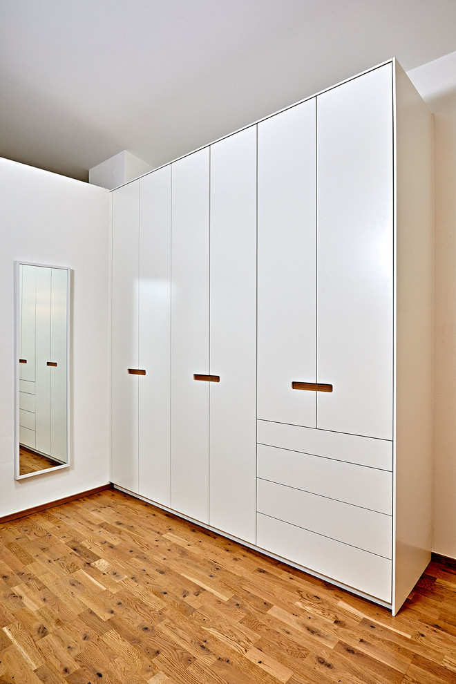Mid-sized trendy gender-neutral medium tone wood floor and brown floor walk-in closet photo in Other with flat-panel cabinets and white cabinets