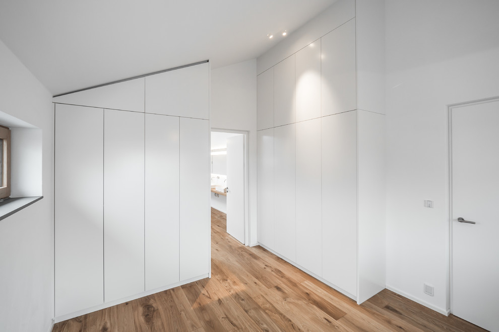 Mittelgroßes, Neutrales Modernes Ankleidezimmer mit Ankleidebereich, flächenbündigen Schrankfronten, weißen Schränken, braunem Holzboden und braunem Boden in Stuttgart