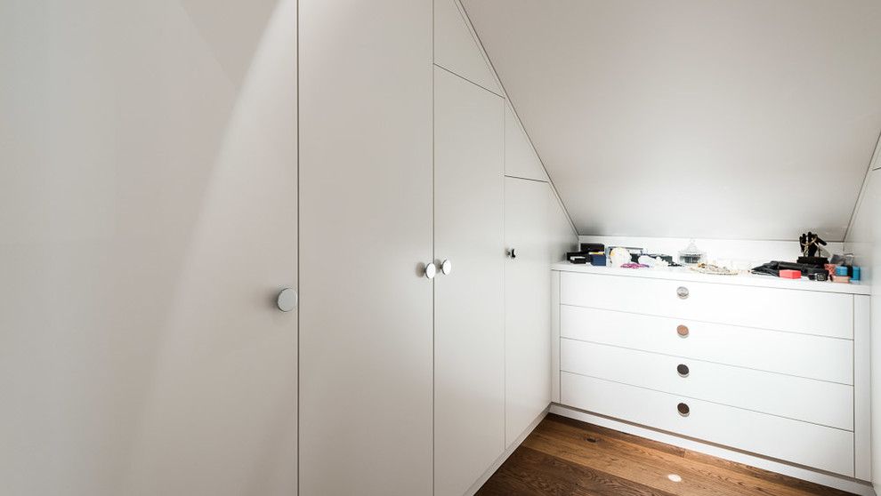 Foto på ett litet funkis walk-in-closet för könsneutrala, med släta luckor, vita skåp, mellanmörkt trägolv och brunt golv