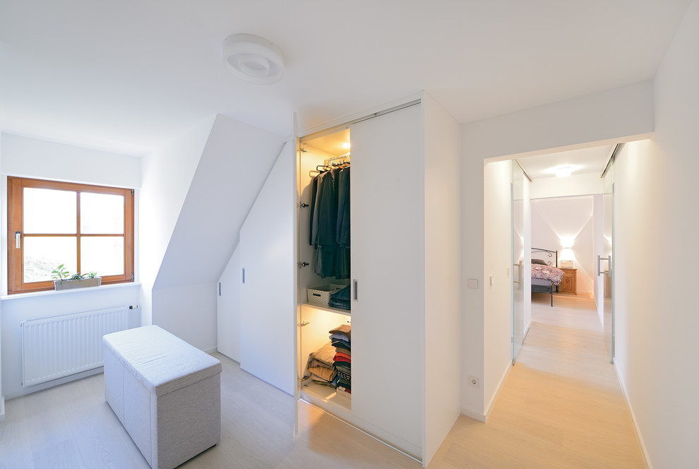 На фото: гардеробная комната среднего размера, унисекс в стиле модернизм с плоскими фасадами, белыми фасадами и светлым паркетным полом с
