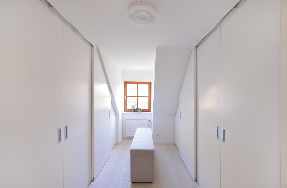 Foto de armario vestidor unisex moderno de tamaño medio con armarios con paneles lisos, puertas de armario blancas y suelo de madera clara
