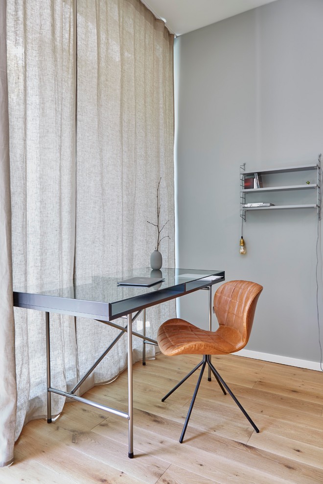 Modelo de despacho actual pequeño sin chimenea con paredes grises, suelo de madera en tonos medios, escritorio independiente y suelo marrón