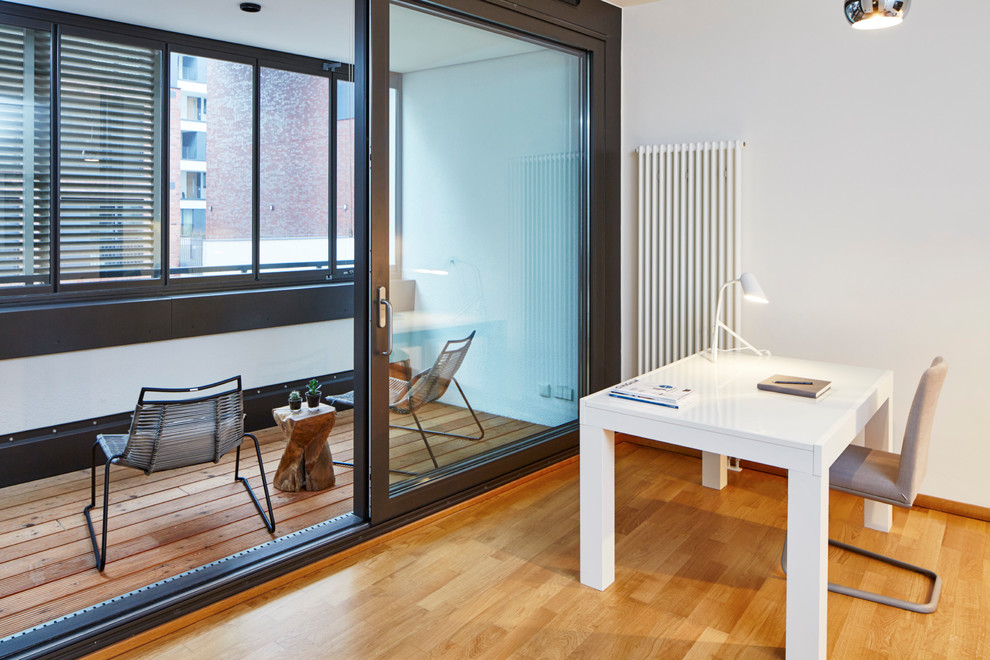 Ejemplo de despacho actual de tamaño medio con paredes blancas, suelo de madera clara y escritorio independiente