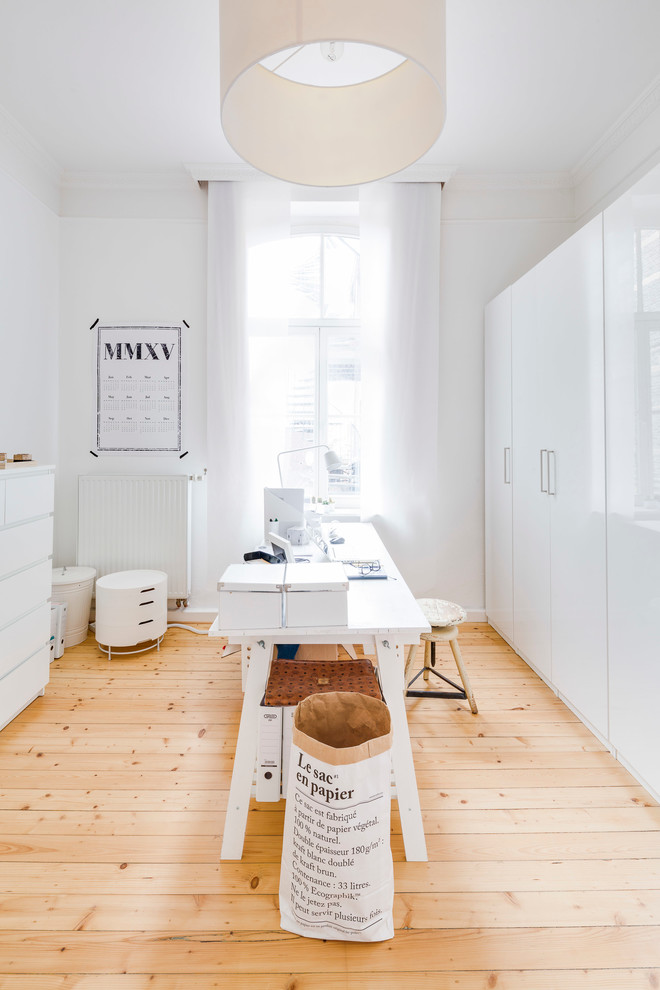 Mittelgroßes Nordisches Arbeitszimmer ohne Kamin mit weißer Wandfarbe, hellem Holzboden, freistehendem Schreibtisch und Arbeitsplatz in Köln