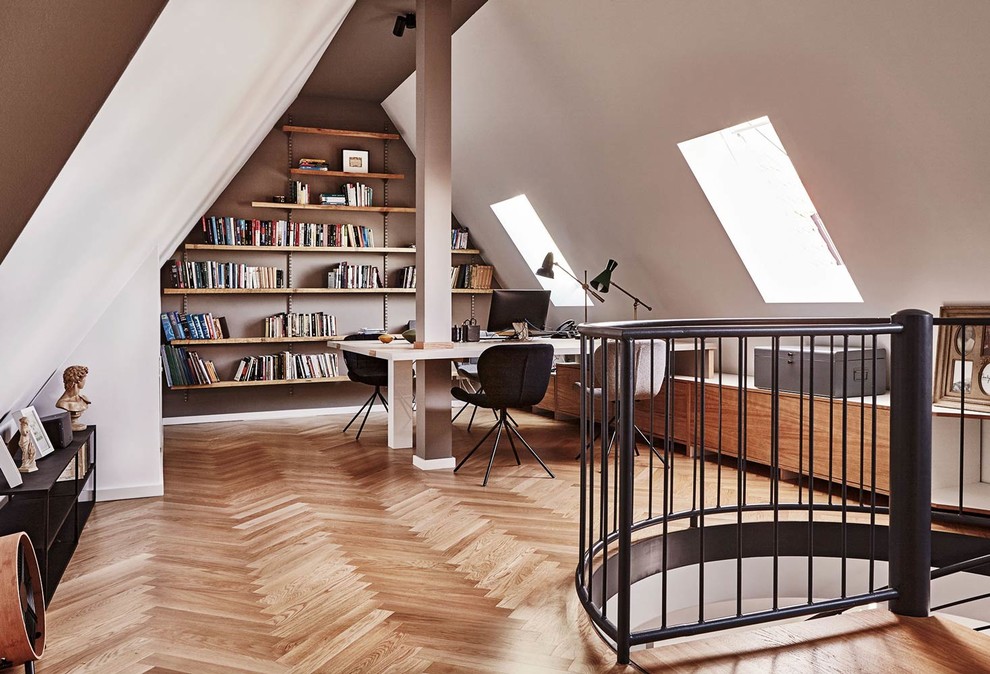 Großes Nordisches Arbeitszimmer ohne Kamin mit Arbeitsplatz, weißer Wandfarbe, braunem Holzboden, freistehendem Schreibtisch und braunem Boden in Berlin