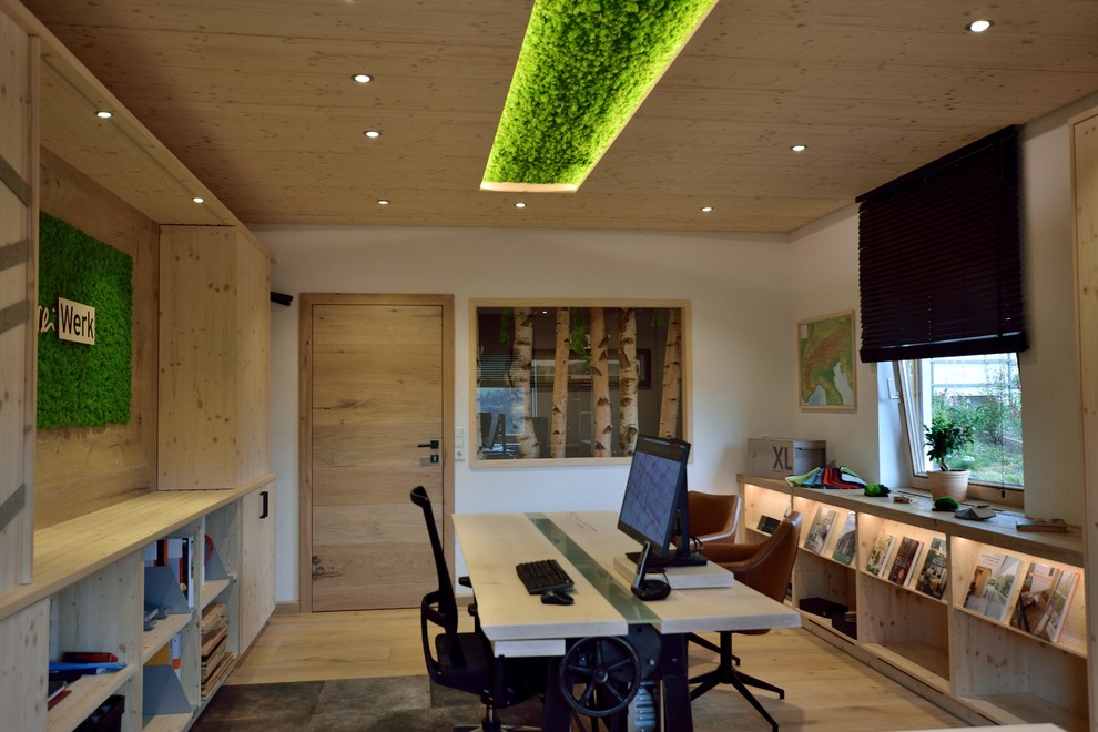Modelo de despacho actual de tamaño medio con paredes blancas, suelo de madera clara, escritorio independiente y suelo beige