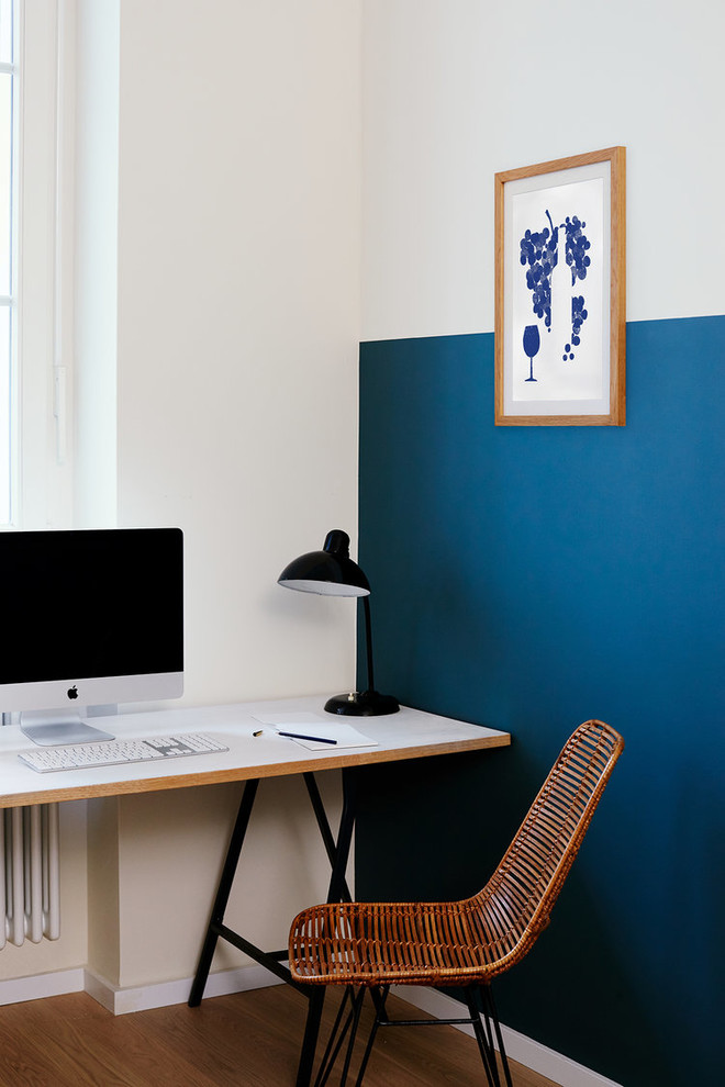 Inredning av ett modernt litet hemmabibliotek, med blå väggar, mellanmörkt trägolv, ett fristående skrivbord och brunt golv
