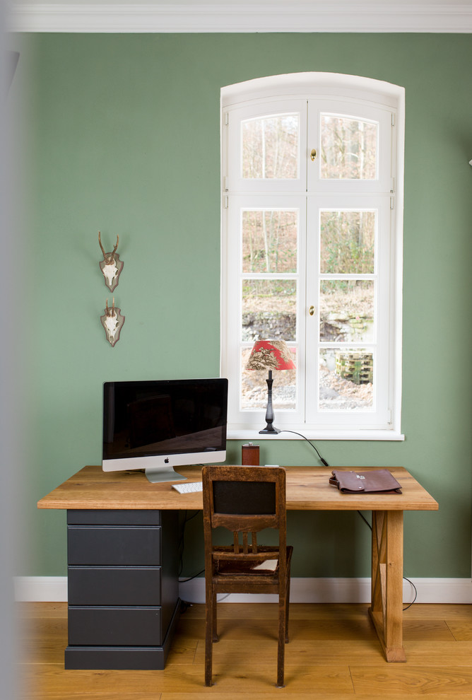 Mittelgroßes Modernes Arbeitszimmer mit Arbeitsplatz, grüner Wandfarbe, hellem Holzboden, freistehendem Schreibtisch und braunem Boden in Sonstige
