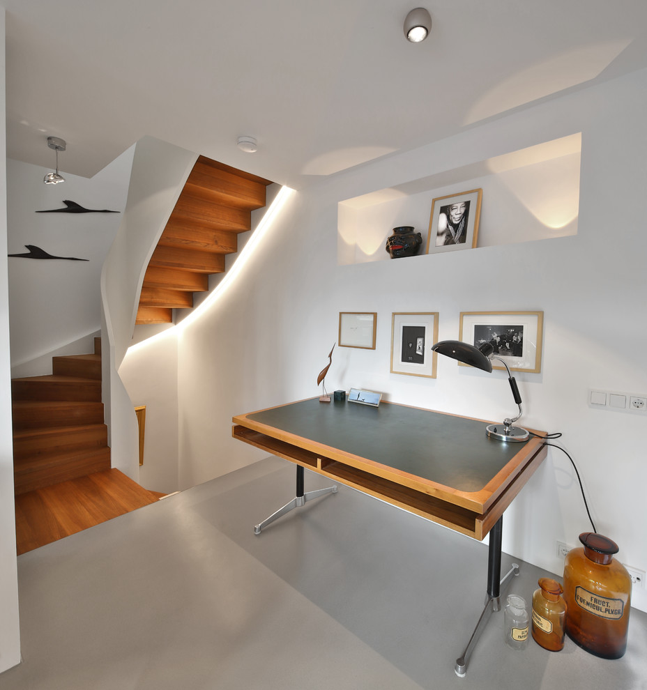 На фото: рабочее место среднего размера в стиле модернизм с белыми стенами, бетонным полом, отдельно стоящим рабочим столом и серым полом без камина с
