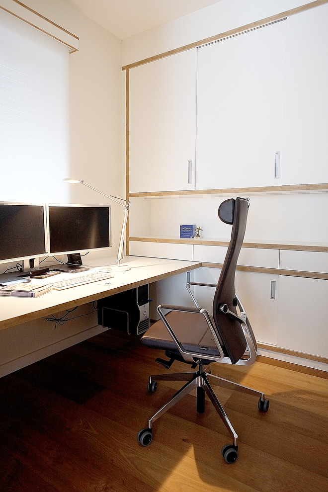 Mittelgroßes Modernes Arbeitszimmer ohne Kamin mit Arbeitsplatz, weißer Wandfarbe, braunem Holzboden, freistehendem Schreibtisch und braunem Boden in Berlin