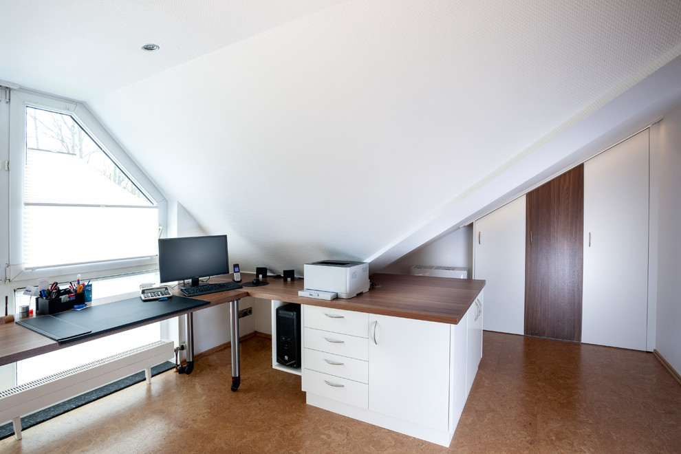 エッセンにある中くらいなコンテンポラリースタイルのおしゃれな書斎 (白い壁、コルクフローリング、造り付け机、茶色い床) の写真