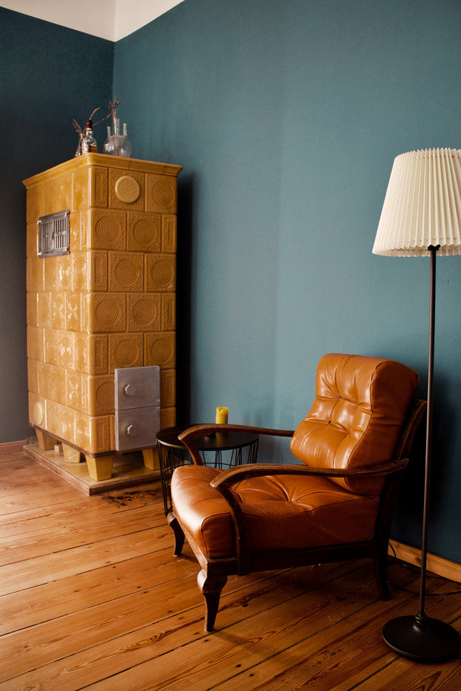 Modelo de despacho vintage grande con biblioteca, paredes azules, suelo de madera en tonos medios, estufa de leña, marco de chimenea de baldosas y/o azulejos, escritorio independiente y suelo marrón