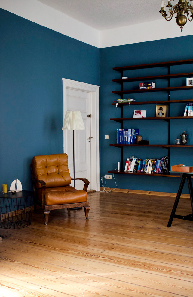 Großes Retro Lesezimmer mit blauer Wandfarbe, braunem Holzboden, Kaminofen, gefliester Kaminumrandung, freistehendem Schreibtisch und braunem Boden in Sonstige
