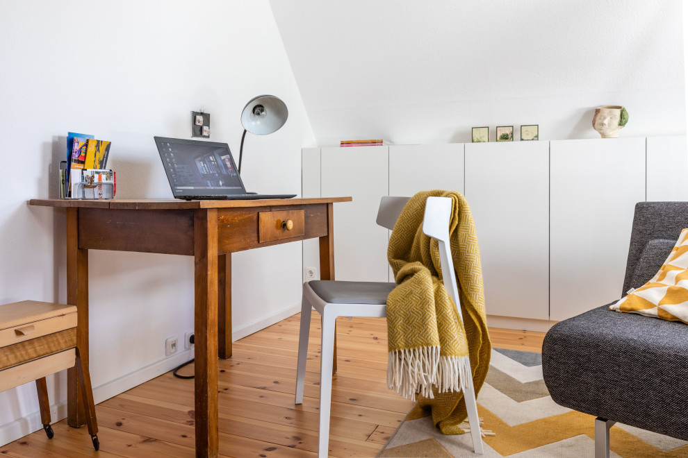 Bild på ett litet minimalistiskt hemmabibliotek, med vita väggar, heltäckningsmatta, ett fristående skrivbord och beiget golv
