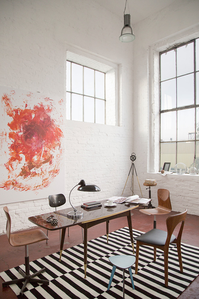 Ejemplo de despacho industrial de tamaño medio sin chimenea con paredes blancas, suelo de cemento, escritorio independiente y suelo rojo