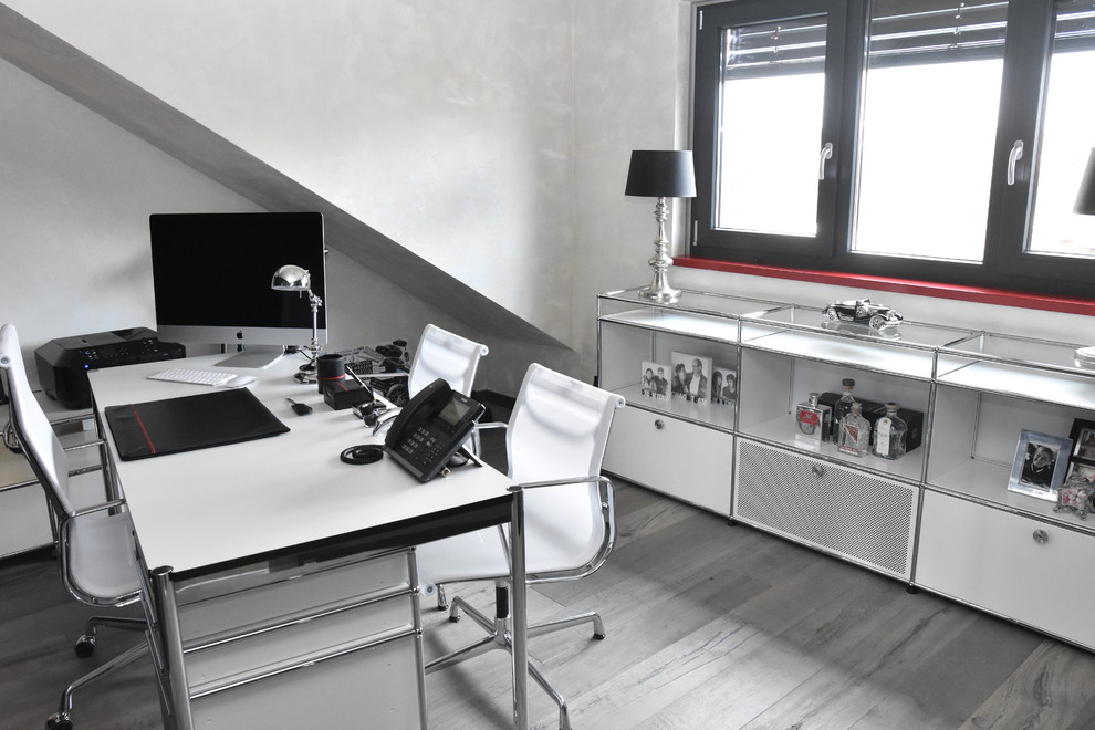 Großes Modernes Arbeitszimmer mit Arbeitsplatz, weißer Wandfarbe, freistehendem Schreibtisch und braunem Holzboden in Dortmund