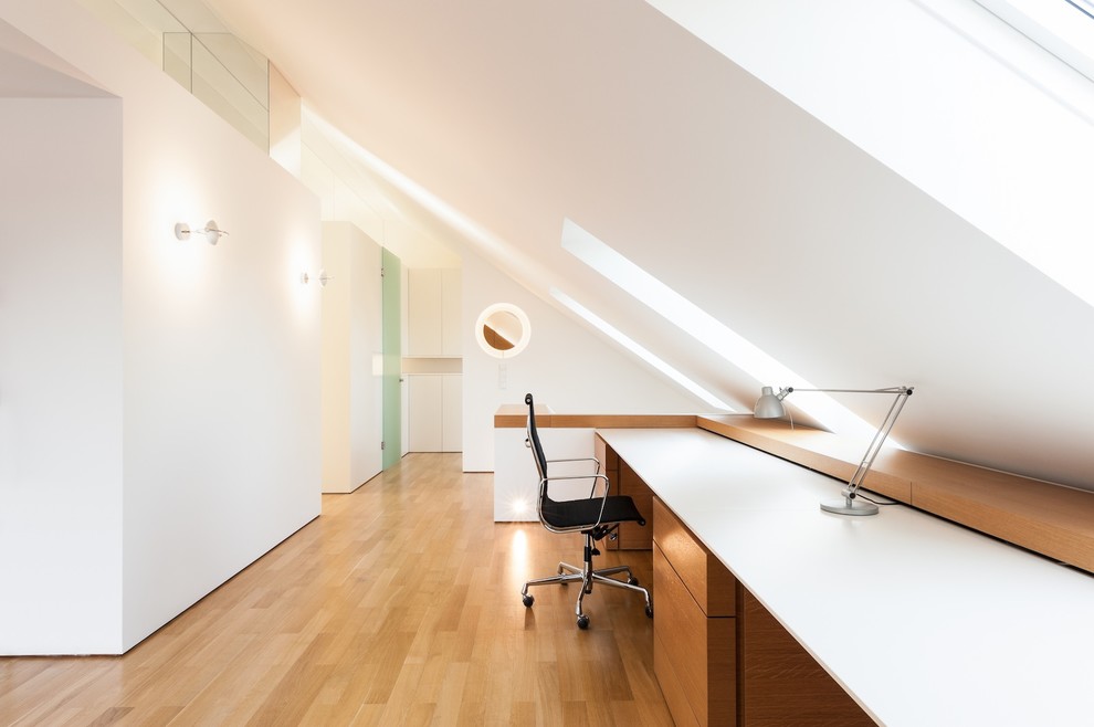 Cette image montre un grand bureau minimaliste avec un mur blanc, un sol en bois brun, aucune cheminée et un bureau intégré.