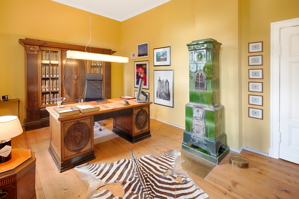 Exempel på ett mellanstort eklektiskt hemmabibliotek, med gula väggar, målat trägolv, en öppen vedspis, en spiselkrans i trä, ett fristående skrivbord och brunt golv