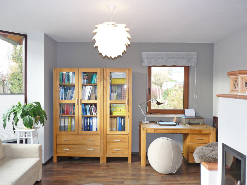 Exemple d'un bureau tendance de taille moyenne avec un mur gris, un sol en bois brun, une cheminée standard, un bureau indépendant et un sol marron.