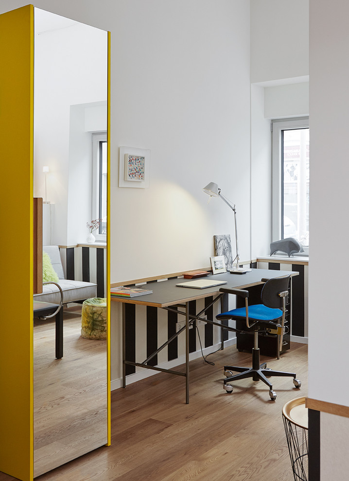 Kleines Modernes Arbeitszimmer ohne Kamin mit Arbeitsplatz, weißer Wandfarbe, hellem Holzboden, freistehendem Schreibtisch und braunem Boden in Düsseldorf