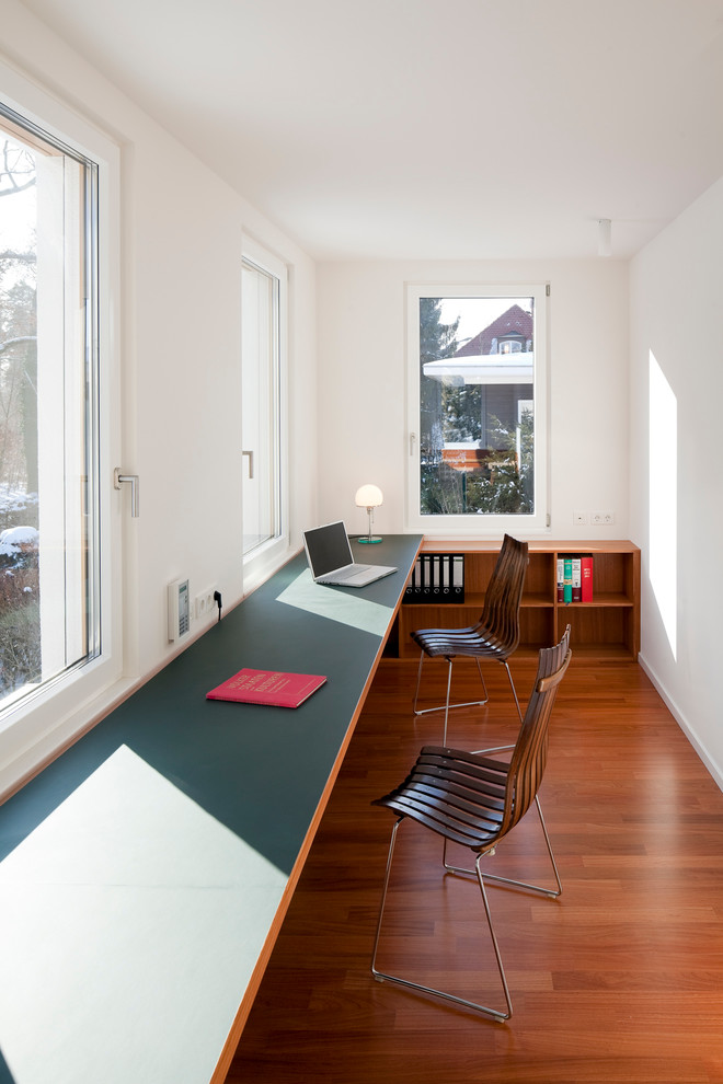 Modelo de despacho contemporáneo de tamaño medio sin chimenea con escritorio empotrado, paredes blancas y suelo de madera en tonos medios