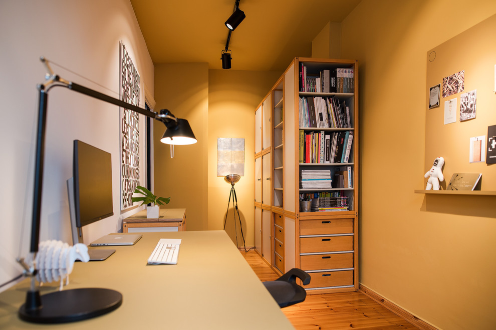 Пример оригинального дизайна: маленькое рабочее место в современном стиле с желтыми стенами, светлым паркетным полом и отдельно стоящим рабочим столом для на участке и в саду