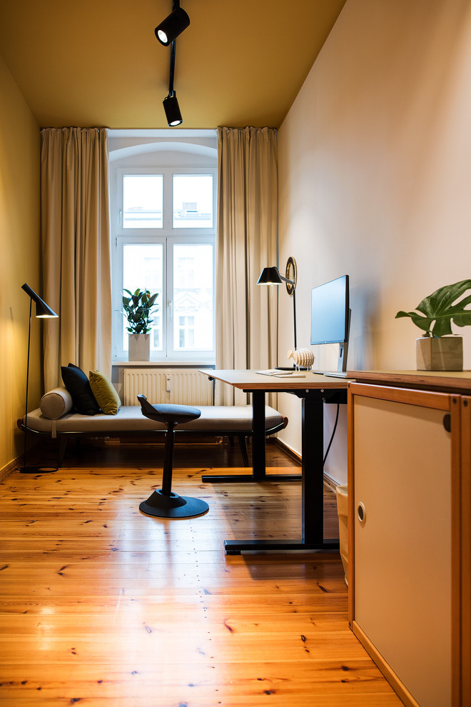 Kleines Modernes Arbeitszimmer mit Arbeitsplatz, gelber Wandfarbe, hellem Holzboden und freistehendem Schreibtisch in Berlin