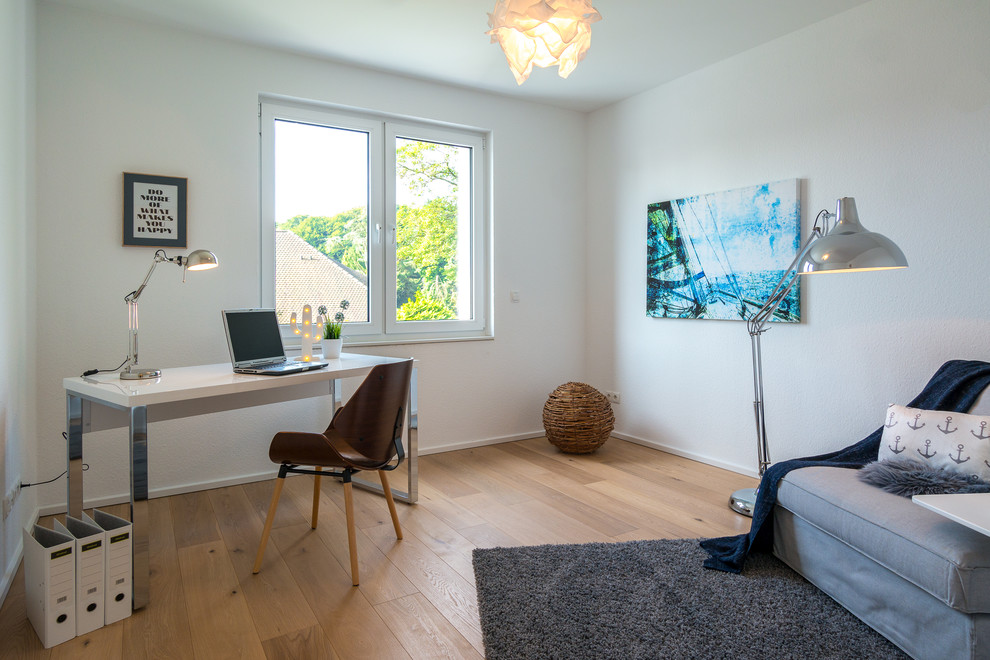 Mittelgroßes Skandinavisches Arbeitszimmer ohne Kamin mit Arbeitsplatz, weißer Wandfarbe, braunem Holzboden, freistehendem Schreibtisch und braunem Boden in Hamburg