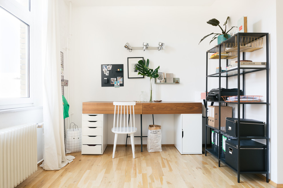 Kleines Mid-Century Arbeitszimmer ohne Kamin mit weißer Wandfarbe, freistehendem Schreibtisch, Arbeitsplatz, hellem Holzboden und braunem Boden in Berlin