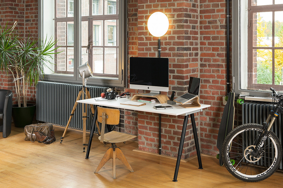 This is an example of an urban study in Essen with no fireplace, a freestanding desk, red walls and light hardwood flooring.