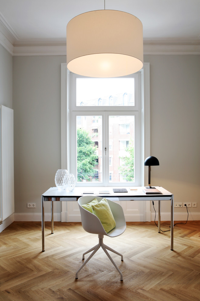 Modelo de despacho actual de tamaño medio sin chimenea con suelo de madera clara, paredes grises y escritorio independiente