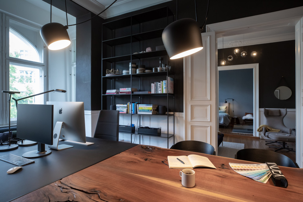 Großes Modernes Arbeitszimmer mit schwarzer Wandfarbe, braunem Holzboden, braunem Boden, Arbeitsplatz und freistehendem Schreibtisch in Berlin