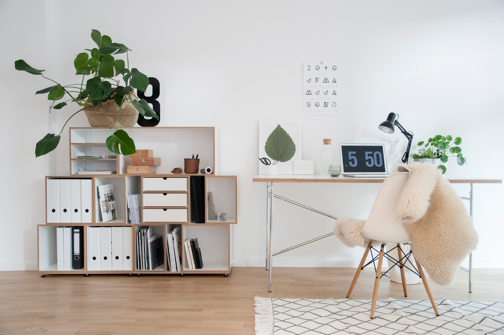 Medium sized scandi study in Berlin with white walls, light hardwood flooring, no fireplace, a freestanding desk and brown floors.