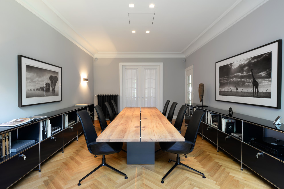 Diseño de despacho contemporáneo grande con paredes grises, suelo de madera clara y escritorio independiente