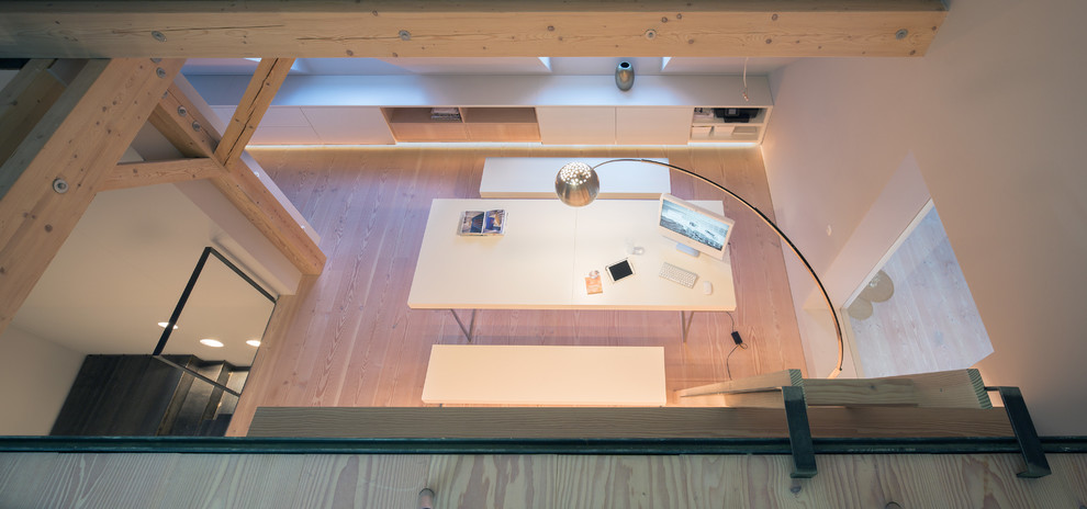 Mittelgroßes Arbeitszimmer mit Arbeitsplatz, weißer Wandfarbe, freistehendem Schreibtisch und braunem Boden in München