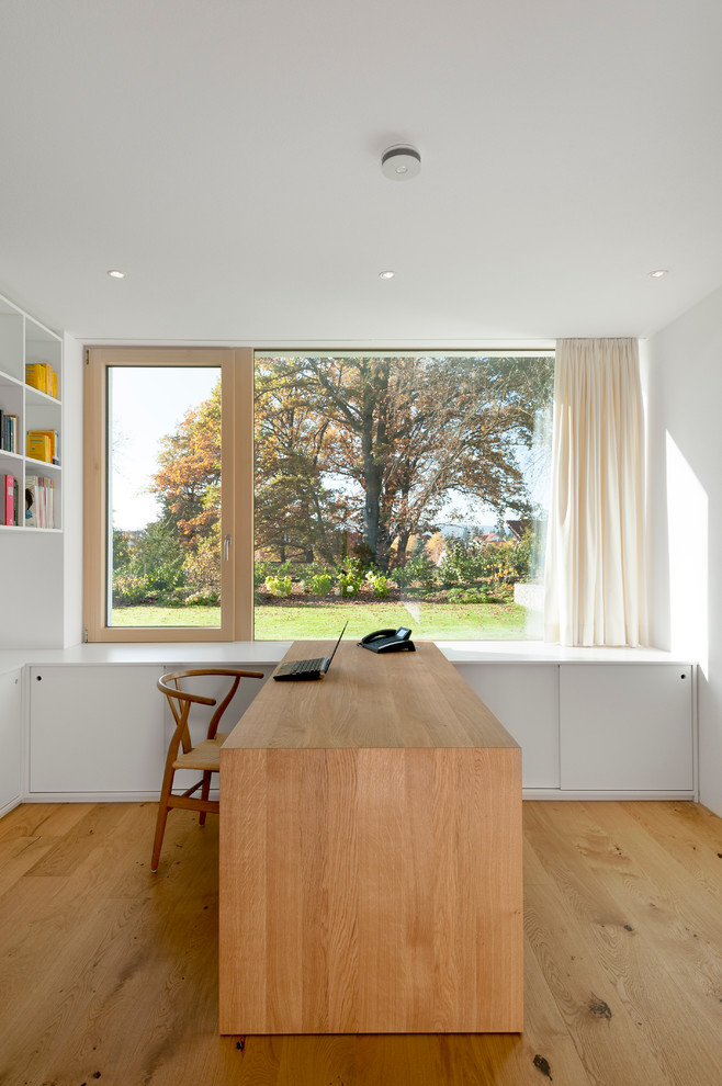 Inspiration för mellanstora moderna hemmabibliotek, med vita väggar, mellanmörkt trägolv och ett fristående skrivbord