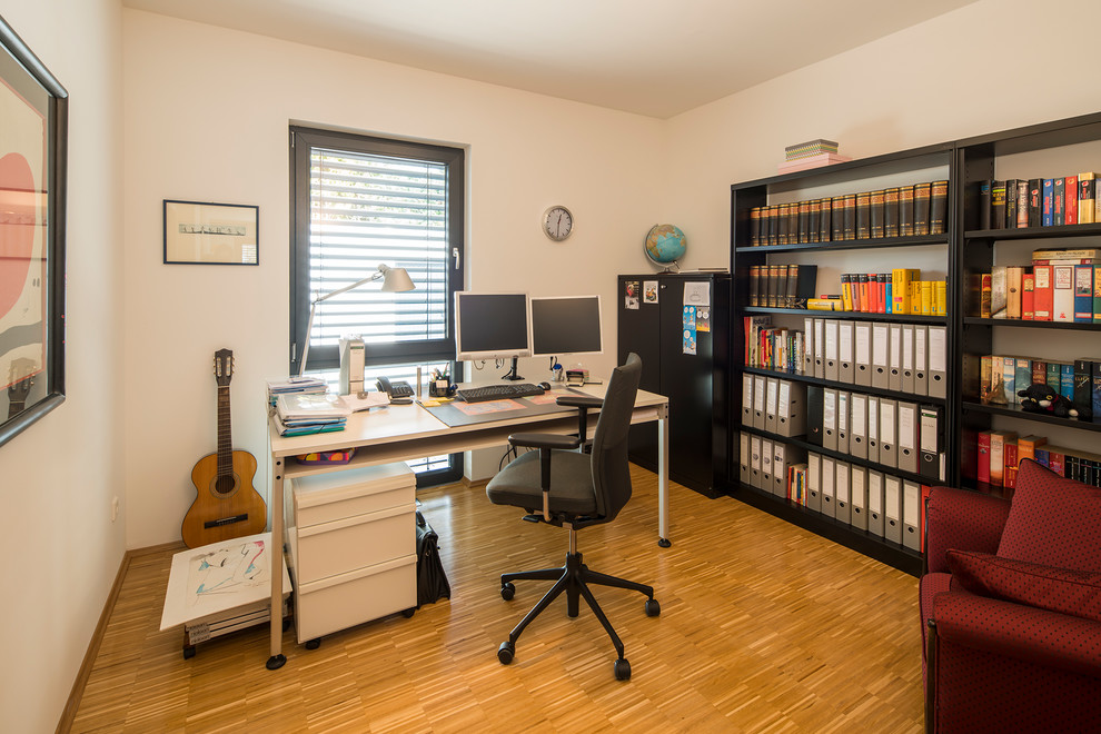 Modernes Arbeitszimmer ohne Kamin mit Arbeitsplatz, weißer Wandfarbe, hellem Holzboden, freistehendem Schreibtisch und braunem Boden in Sonstige