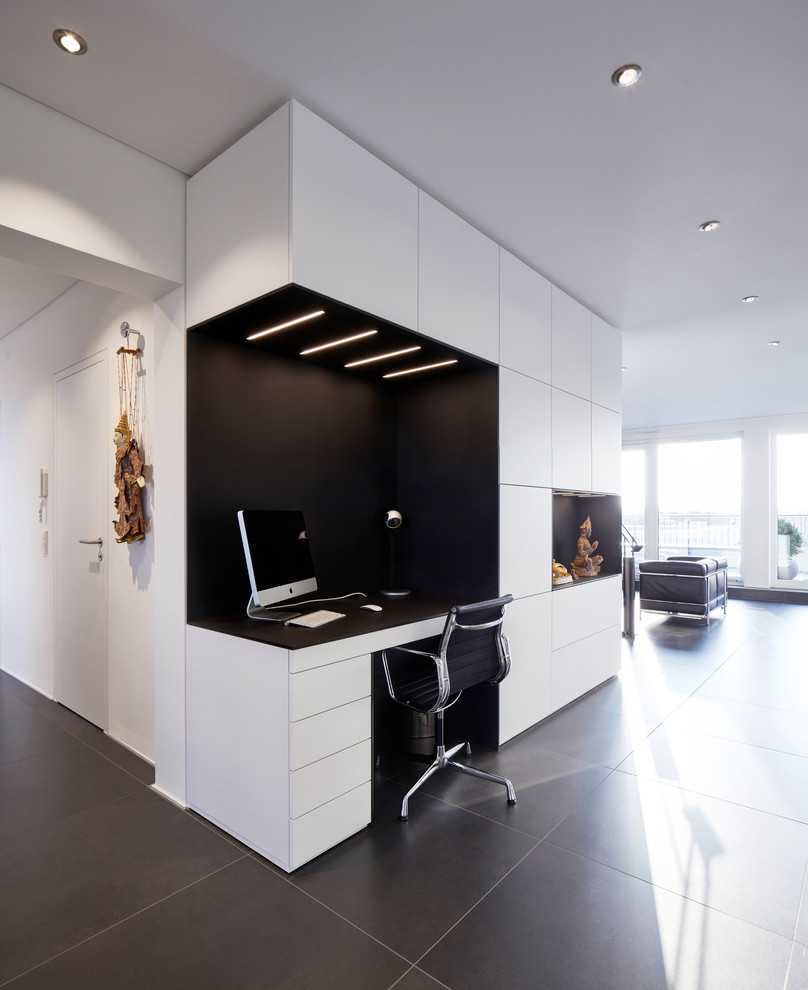 На фото: рабочее место среднего размера в стиле модернизм с белыми стенами, встроенным рабочим столом и черным полом без камина с