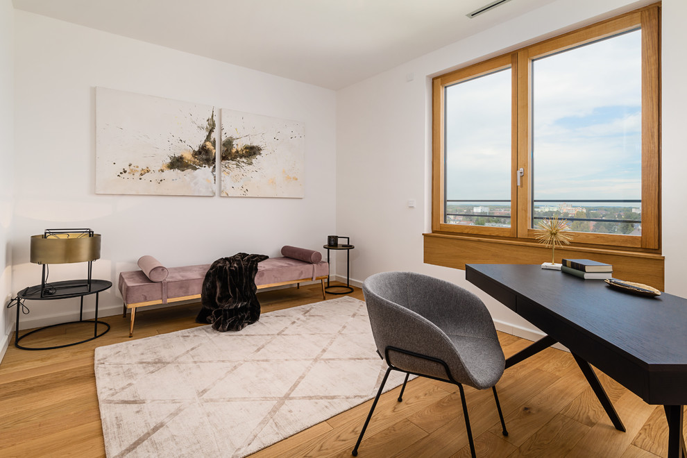 Mittelgroßes Modernes Arbeitszimmer ohne Kamin mit Arbeitsplatz, weißer Wandfarbe, braunem Holzboden, freistehendem Schreibtisch und braunem Boden in München