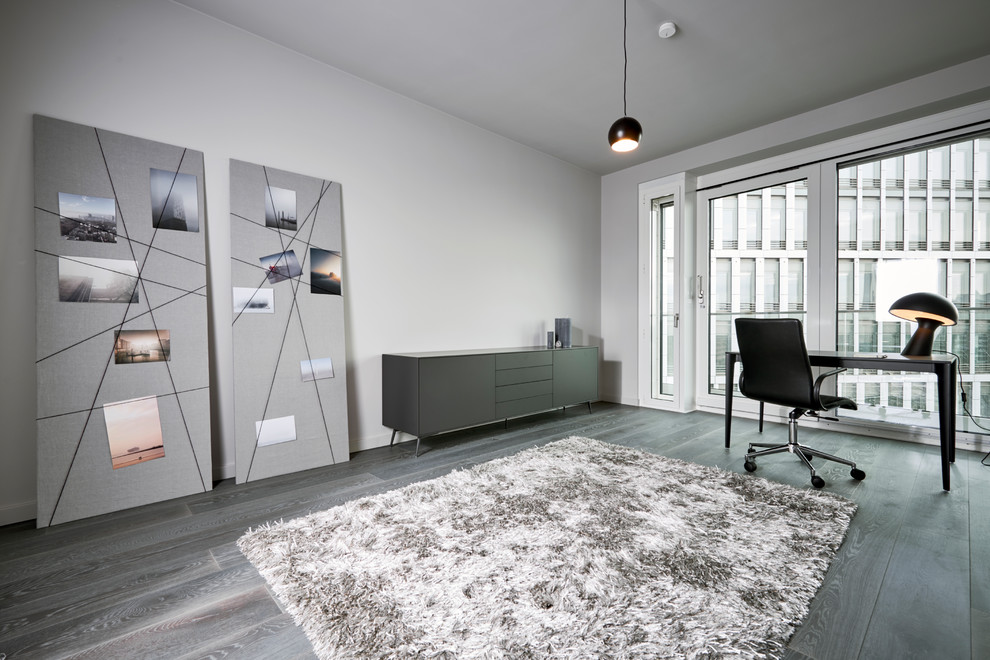 Mittelgroßes Modernes Arbeitszimmer mit Arbeitsplatz, grauer Wandfarbe, freistehendem Schreibtisch, grauem Boden und dunklem Holzboden in Hamburg