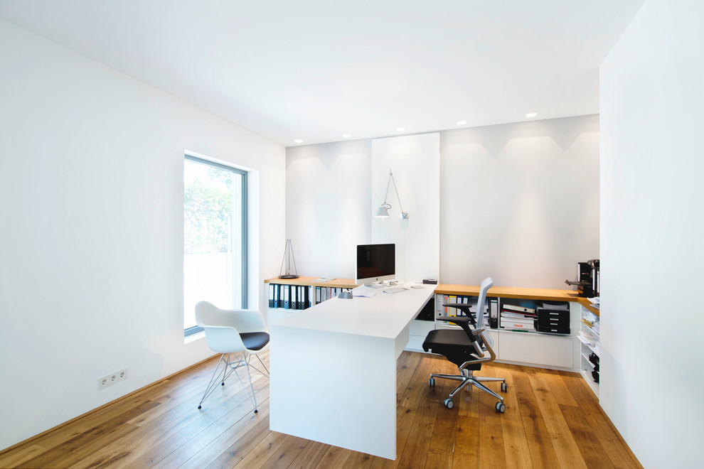 Großes Modernes Arbeitszimmer ohne Kamin mit Einbau-Schreibtisch, Arbeitsplatz, weißer Wandfarbe und braunem Holzboden in Nürnberg