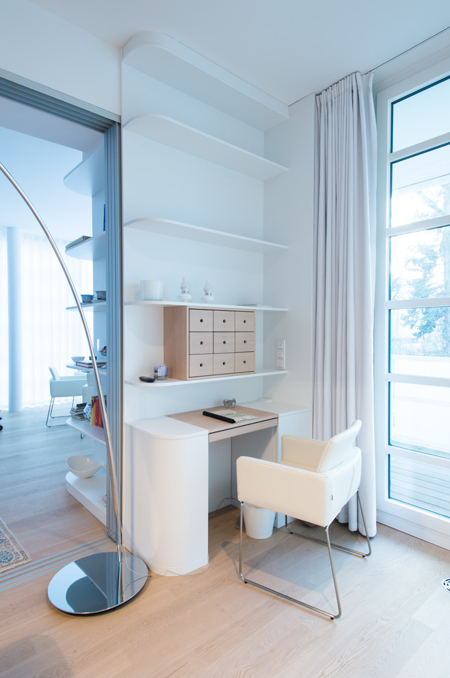 Immagine di un piccolo ufficio design con pareti bianche, parquet chiaro e scrivania incassata