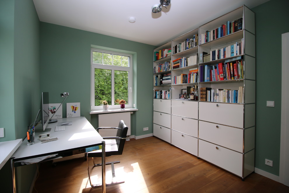 Mittelgroßes Retro Arbeitszimmer ohne Kamin mit Arbeitsplatz, grüner Wandfarbe, hellem Holzboden, freistehendem Schreibtisch und braunem Boden in Frankfurt am Main