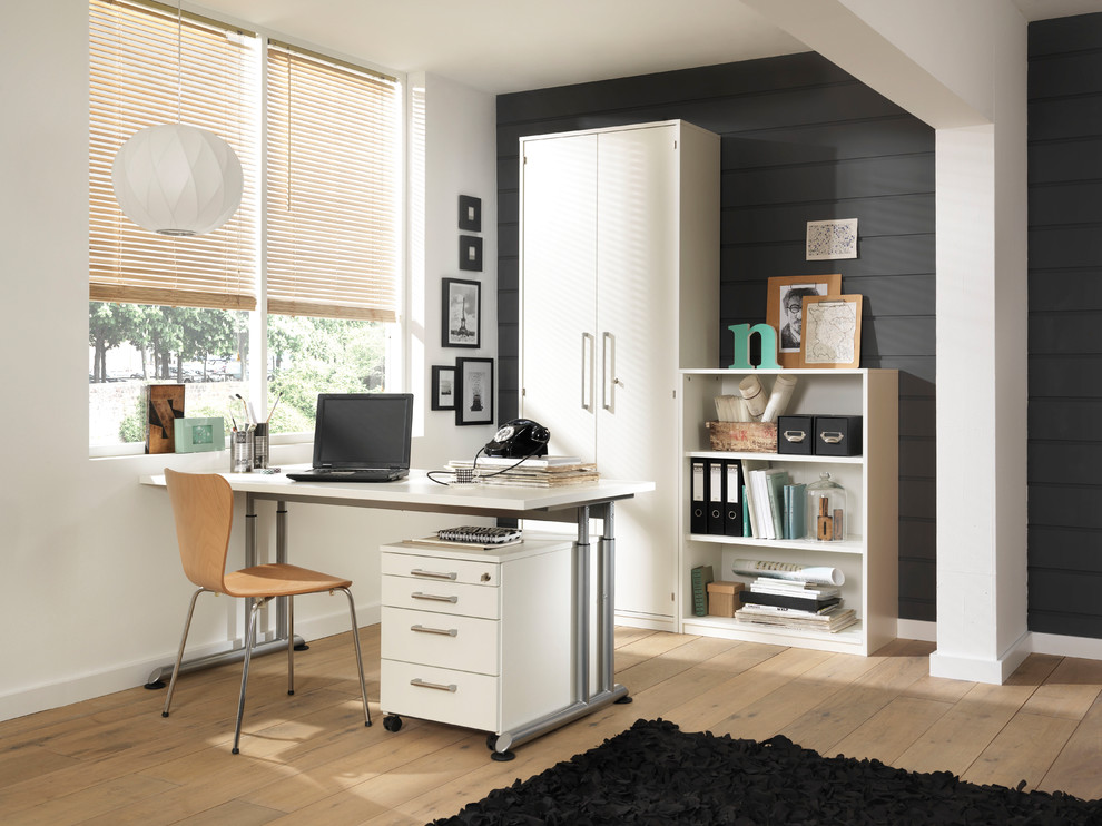 Diseño de despacho actual de tamaño medio sin chimenea con paredes blancas, suelo de madera clara, escritorio independiente y suelo beige