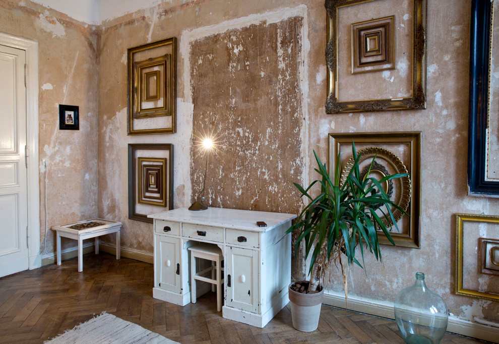 Modelo de despacho bohemio grande sin chimenea con paredes beige, suelo de madera en tonos medios y escritorio independiente
